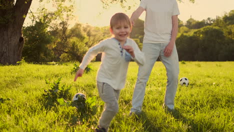 A-young-father-in-a-white-t-shirt-with-two-sons-playing-football-on-the-grass-at-sunset-in-the-sun-in-slow-motion